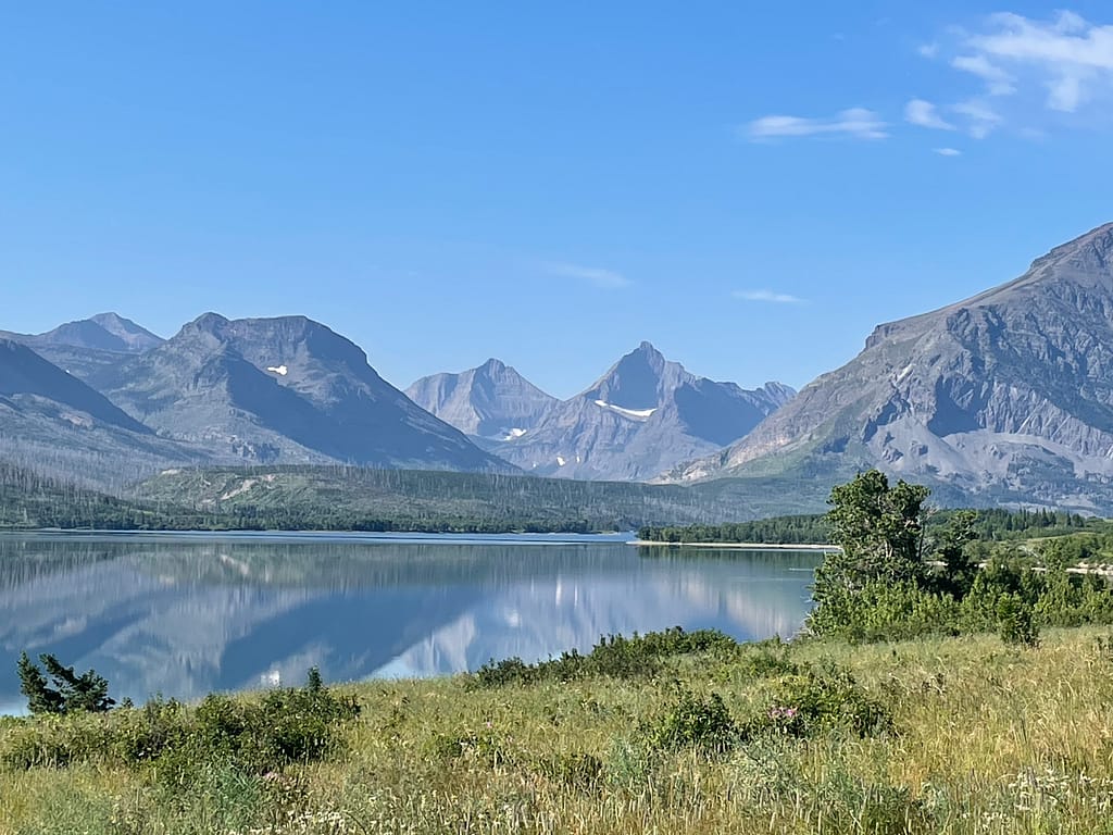 Mountains, snow, reflective lake, grass, trees, Glacier National Park, Montana